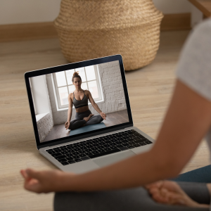 Woman practicing private online yoga at home guided by a live virtual yoga session on a laptop.
