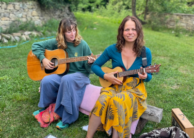 Two people playing guitar and ukulele in a natural setting, evoking connection, creativity, and a sense of ease during a group retreat.