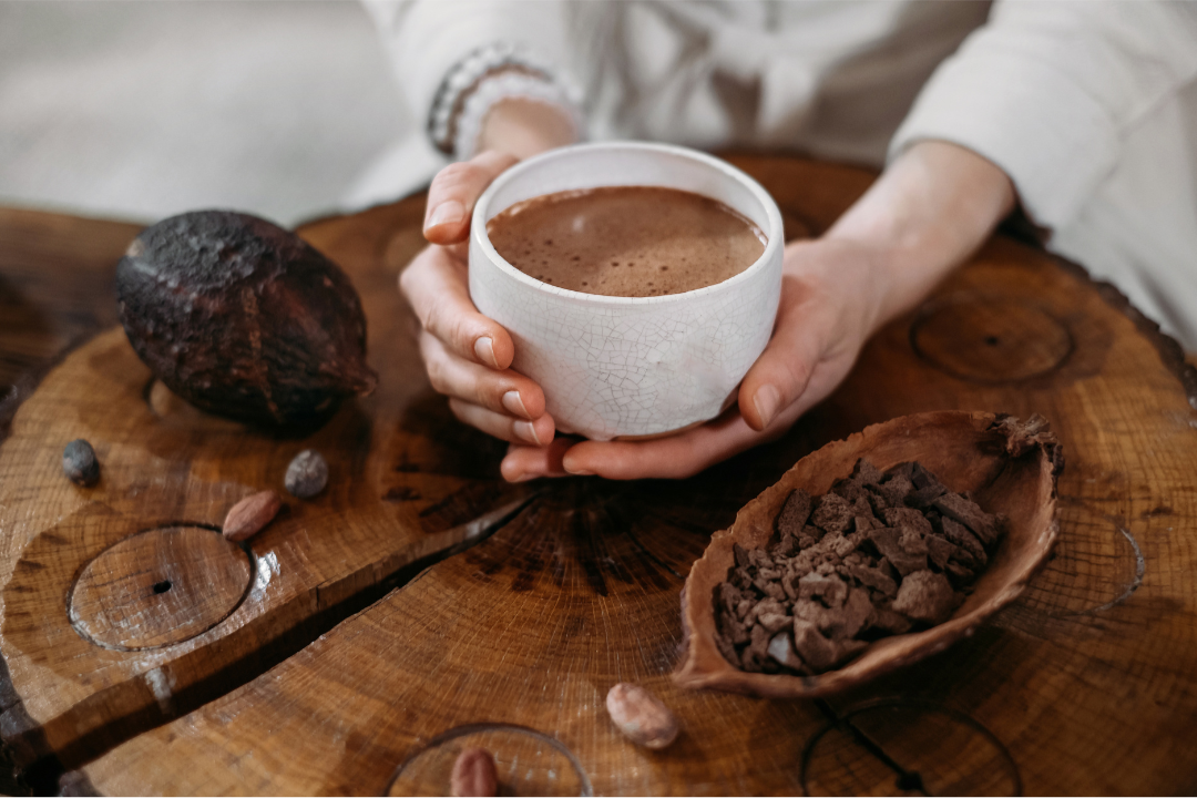 A hand gently holding a cup of ceremonial cacao, symbolising heart-opening ritual, presence, and connection within a sacred practice.