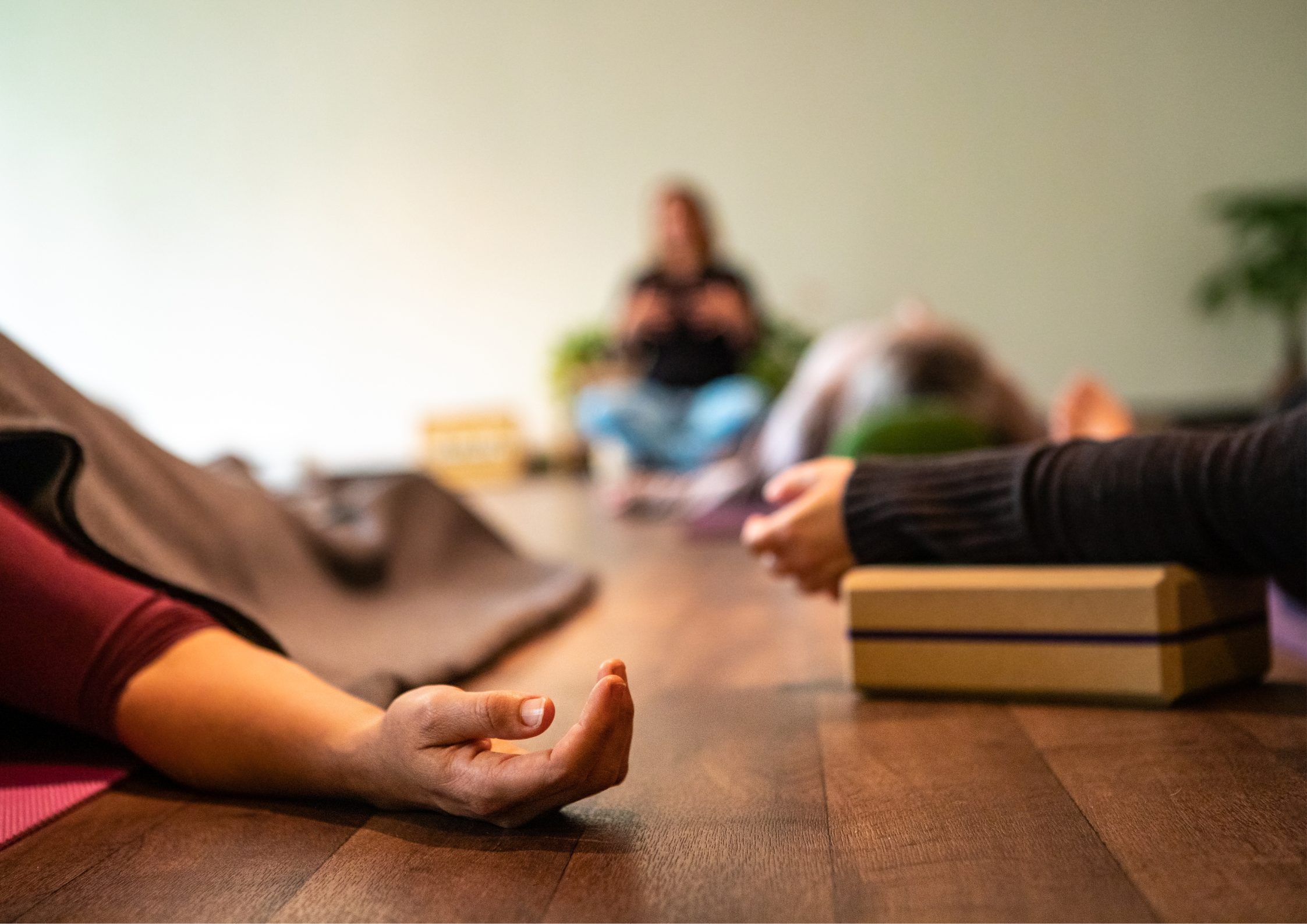 A small group lying in savasana during a Yoga Nidra session, resting deeply in a calm and supportive space.